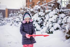 Kleines entzückendes Mädchen spielt an einem Wintertag mit Schneeschaufeln foto