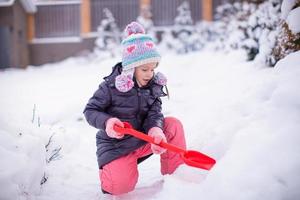 Kleines entzückendes Mädchen spielt an einem Wintertag mit Schneeschaufeln foto