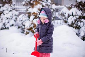 Kleines Mädchen spielt an einem Wintertag mit dem Schneeschaufeln foto