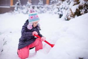 Kleines Mädchen spielt an einem Wintertag mit dem Schneeschaufeln foto