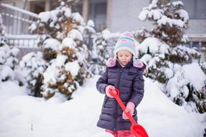 Kleines Mädchen spielt an einem Wintertag mit dem Schneeschaufeln foto