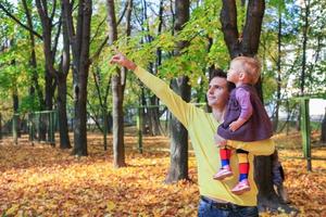 Der junge Vater zeigt seine kleine süße Tochter im Herbstpark im Freien am Himmel foto