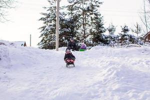 Kleines süßes Mädchen zieht an warmen Wintertagen einen Schlitten foto