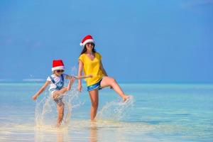 kleines Mädchen und junge Mutter in Weihnachtsmütze während des Strandurlaubs foto