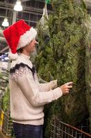 junger mann, der grünen weihnachtsbaum auf dem markt kauft foto