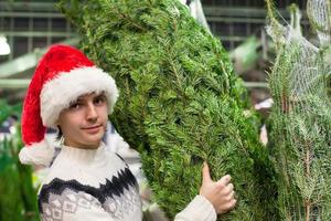 junger mann, der einen weihnachtsbaum im geschäft kauft foto