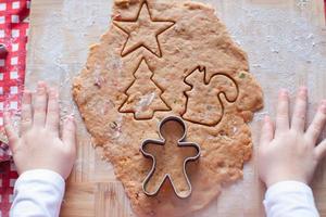 Kinderhände, die vom Teig-Lebkuchenmann für Weihnachten machen foto