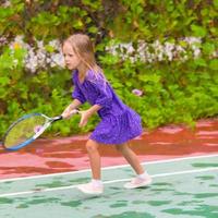 kleines Mädchen, das auf dem Platz Tennis spielt foto