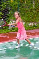 kleines Mädchen, das auf dem Platz Tennis spielt foto