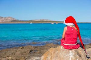 entzückendes kleines mädchen in weihnachtsmütze während des strandurlaubs foto