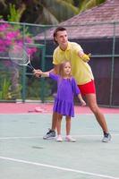 kleines Mädchen, das mit ihrem Vater auf dem Platz Tennis spielt foto