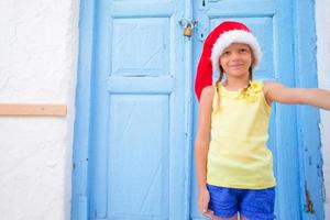 entzückendes kleines mädchen in weihnachtsmütze, das selfie in der schmalen straße im griechischen dorf macht foto