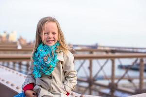 entzückendes kleines Mädchen, das an der Brooklyn Bridge sitzt foto
