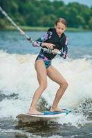 aktives schönes Mädchen im Badeanzug, das auf dem Wakeboard im Fluss steht foto