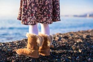 Nahaufnahme der Beine kleines Mädchen in gemütlichen Pelzstiefeln Hintergrund das Meer foto