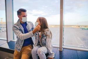 Vater und kleines Mädchen mit medizinischen Masken am Flughafen. Schutz vor Coronavirus und Grip foto