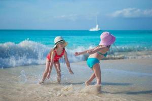 entzückende kleine Mädchen, die im flachen Wasser am exotischen Strand spielen foto