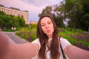 junges Mädchen, das Video-Selfie macht und Spaß im Park hat. Lifestyle-Selfie-Porträt einer jungen positiven Frau, die Spaß hat und sich selbst macht. Konzeptspaß mit neuen Trends und Technologien. foto
