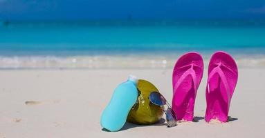 Flip Flops, Kokosnuss und Sonnencreme auf weißem Sand foto