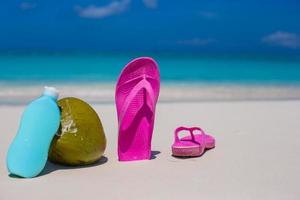 Flip Flops, Kokosnuss und Sonnencreme auf weißem Sand foto