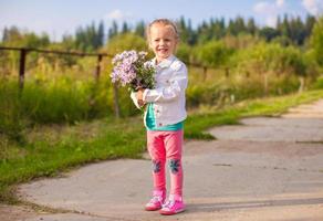 kleines entzückendes mädchen, das draußen mit blumen geht foto