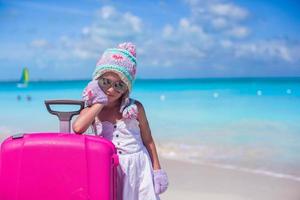 Kleines entzückendes Mädchen in warmer Wintermütze und Fäustlingen an einem tropischen Strand foto