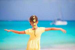 entzückendes kleines Mädchen mit Frangipani-Blüten im Haar am Strand foto