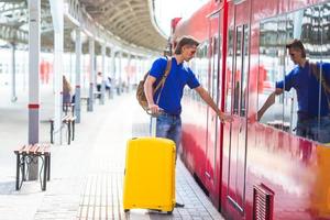 junger Mann mit Gepäck an einem Bahnhof in der Nähe des Schnellzugs foto