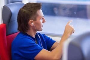 junger kaukasischer mann, der musik hört, schaut auf das fenster, das mit dem zug reist foto