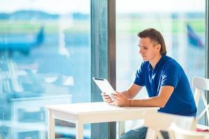 junger mann, der mit laptop im flughafencafé arbeitet und auf das einsteigen wartet foto