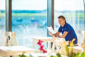 junger mann, der mit laptop im flughafencafé arbeitet und auf das einsteigen wartet foto