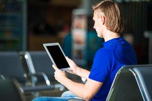 junger Mann mit Laptop am Flughafen, während er auf das Boarding wartet foto