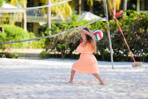 Kleines entzückendes Mädchen, das Volleyball am Strand mit Ball spielt foto