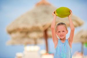 Kleines entzückendes Mädchen mit Kokosnuss am weißen tropischen Strand foto