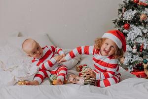 kinder in rot-weißen pyjamas essen weihnachtsbonbons im bett. bruder und schwester, junge und mädchen teilen geschenke. Weihnachtsmorgen. Lebensstil. Platz für Text. hochwertiges Foto