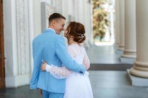 Braut in einem leichten Hochzeitskleid zum Bräutigam in einem blauen Anzug foto