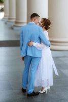 Braut in einem leichten Hochzeitskleid zum Bräutigam in einem blauen Anzug foto