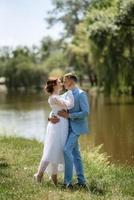 Braut in einem leichten Hochzeitskleid zum Bräutigam in einem blauen Anzug foto