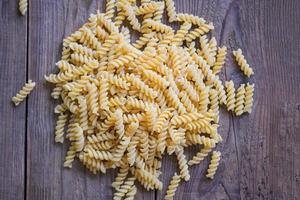 rohe Nudeln Makkaroni auf Holzhintergrund, Nahaufnahme rohe Makkaroni Spiralnudeln ungekochte köstliche Fusilli-Nudeln zum Kochen von Speisen foto