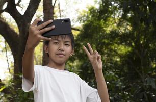 Gruppe junger asiatischer Teenager, die Freizeit im Park verbringen, ihre Finger heben und glücklich zusammen Selfie machen, weicher und selektiver Fokus auf Jungen im weißen T-Shirt, Teenager-Konzept aufziehen. foto