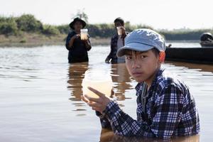 Der junge asiatische Junge hält ein transparentes Rohr, in dem sich Beispielwasser befindet, um das Experiment und die pH-Wert-Messung durchzuführen, während sein Schulprojekt mit seinen Freunden hinter dem Fluss arbeitet, an dem er lebte. foto