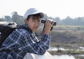 Der asiatische Junge benutzt ein Fernglas, um während des Sommercamps die Vögel im tropischen Wald zu beobachten, eine Idee, um Kreaturen und Wildtiere und Insekten außerhalb des Klassenzimmers zu lernen. foto