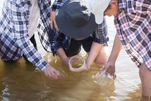 Der junge asiatische Junge hält ein transparentes Rohr, in dem sich Beispielwasser befindet, um das Experiment und die pH-Wert-Messung durchzuführen, während sein Schulprojekt mit seinen Freunden hinter dem Fluss arbeitet, an dem er lebte. foto