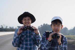 asiatische Jungs benutzen Ferngläser, um während des Sommercamps Vögel im tropischen Wald zu beobachten, eine Idee, um Kreaturen und wild lebende Tiere und Insekten außerhalb des Klassenzimmers zu lernen. foto