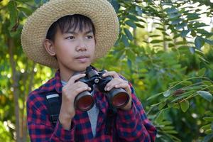 Der asiatische Junge benutzt ein Fernglas, um während des Sommercamps die Vögel im tropischen Wald zu beobachten, eine Idee, um Kreaturen und Wildtiere und Insekten außerhalb des Klassenzimmers zu lernen. foto