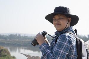 Der asiatische Junge benutzt ein Fernglas, um während des Sommercamps die Vögel im tropischen Wald zu beobachten, eine Idee, um Kreaturen und Wildtiere und Insekten außerhalb des Klassenzimmers zu lernen. foto