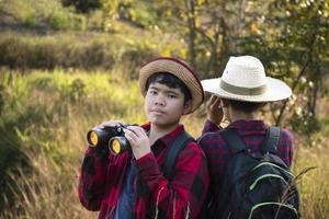 asiatische Jungs benutzen Ferngläser, um während des Sommercamps Vögel im tropischen Wald zu beobachten, eine Idee, um Kreaturen und wild lebende Tiere und Insekten außerhalb des Klassenzimmers zu lernen. foto