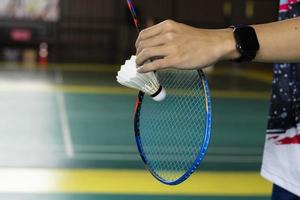 Badmintonspieler hält Federball und Schläger aus weißer Creme vor das Netz, bevor er es auf einer anderen Seite des Platzes serviert, weicher und selektiver Fokus auf Federball. foto