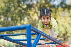 süßes asiatisches mädchenlächeln spielen klettern die bar auf schul- oder kindergartenhof oder spielplatz. gesunde aktivität kinder. kleines Mädchen, das draußen auf dem Spielplatz klettert. Kind spielt auf Spielplatz im Freien. foto