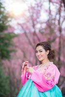 hanbok, das traditionelle koreanische kleid und das schöne asiatische mädchen mit sakura foto